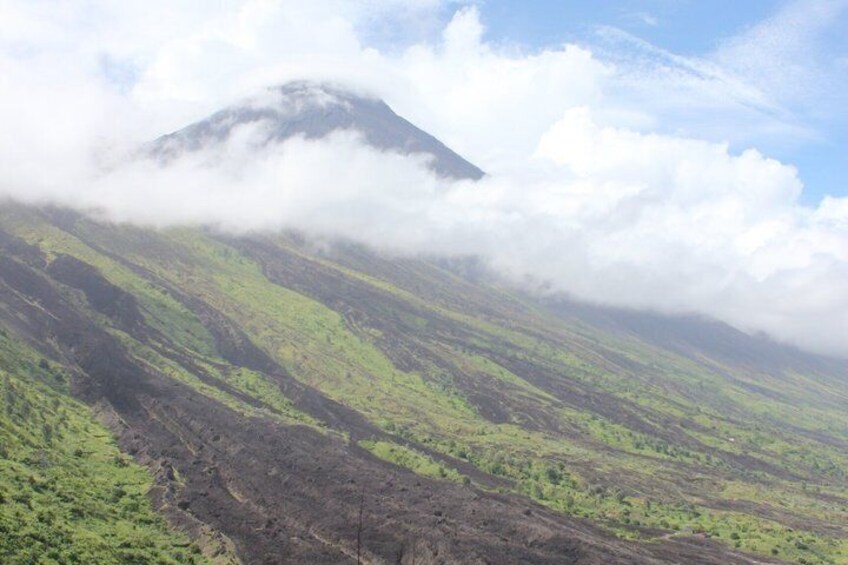 A mountain partially obscured by clouds, with green vegetation on its slopes. 1
