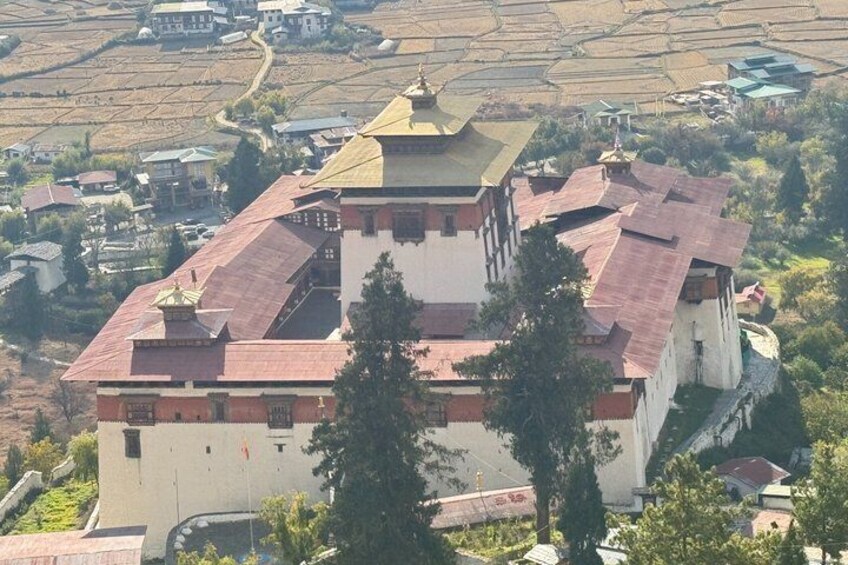A large building with a red roof and a golden spire, surrounded by trees and fields. 1