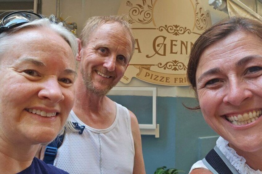 Three people in front of a wall with a pizza sign. 1