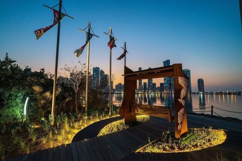 A waterfront promenade with a wooden walkway, decorative flags, and a city skyline in the background. 4