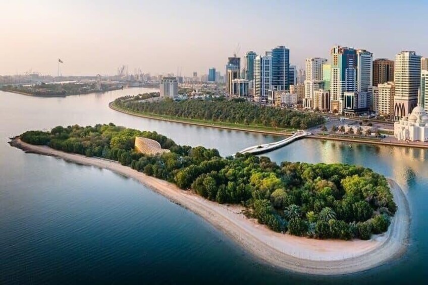 A coastal cityscape with modern high-rise buildings, a curved island with dense greenery, and a calm body of water. 1