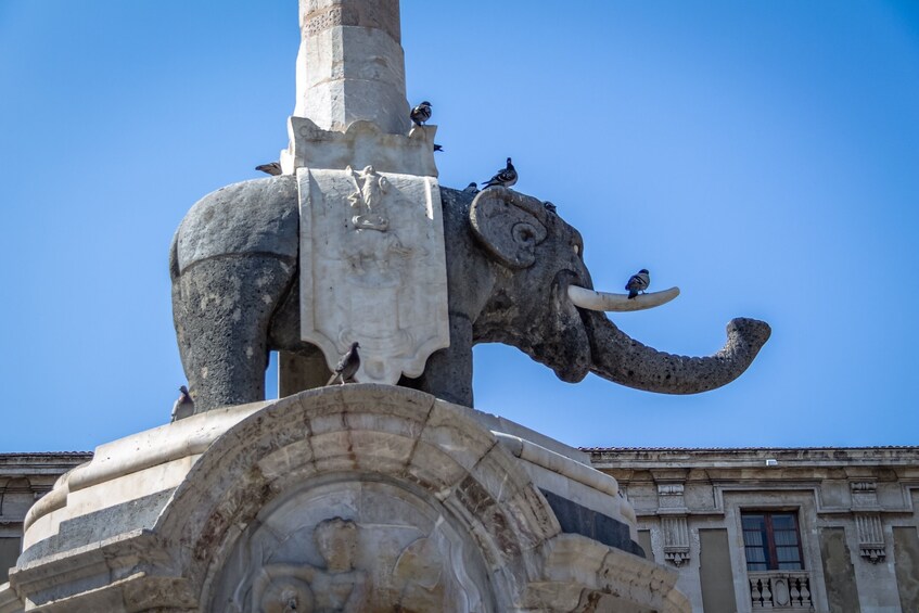 A large elephant statue with birds perched on it, set against a clear blue sky. 5