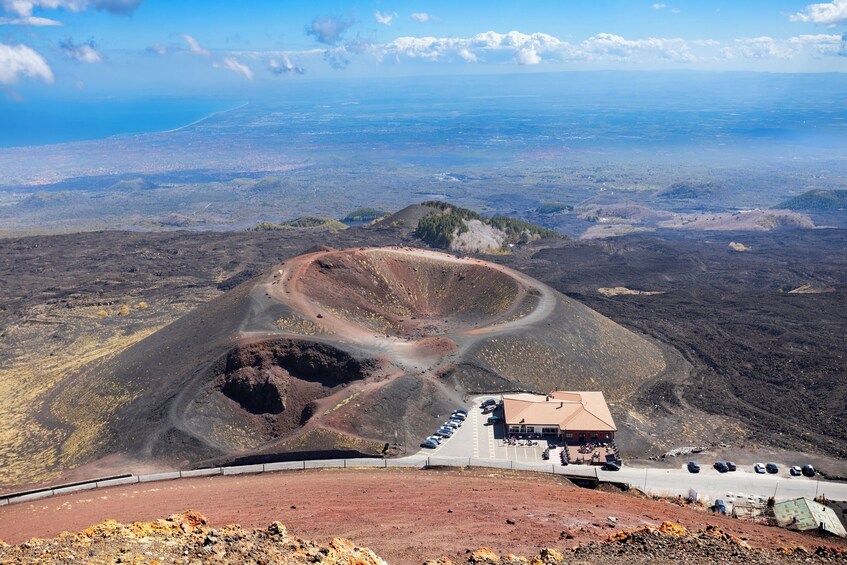 A volcanic crater with a road leading to a building with parked cars. 3