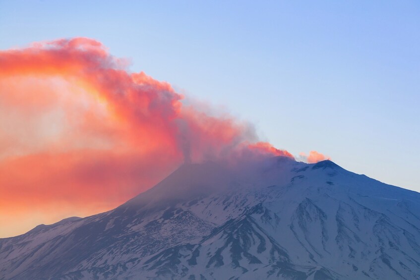 A snow-covered mountain with a plume of smoke or steam rising from its peak. 1