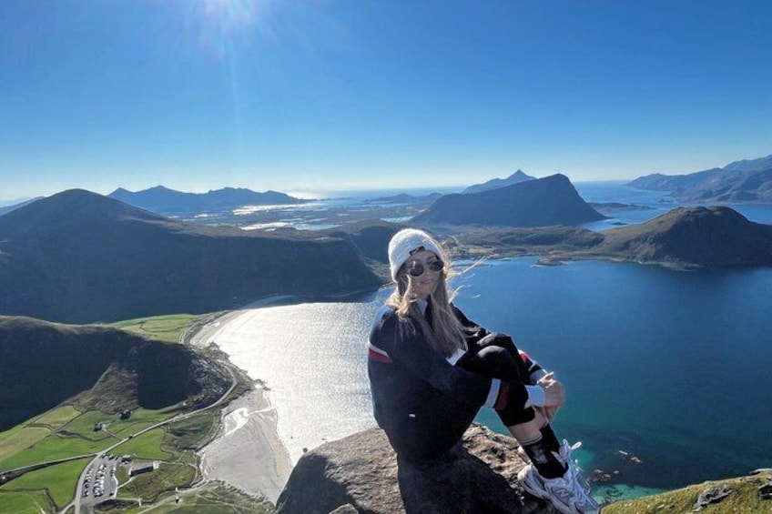 A person standing on a cliff overlooking a coastal landscape with mountains and a bay. 1