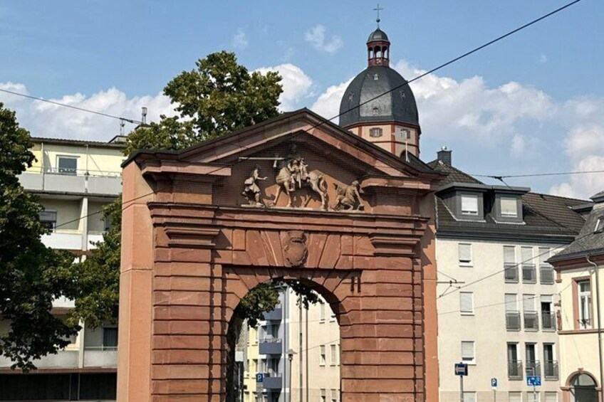 A historical archway with classical relief sculptures, a dome-topped building in the background, and residential buildings. 3