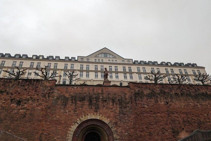 A large building with a flat roof and multiple windows, situated on a brick wall with a circular archway at the bottom. 4