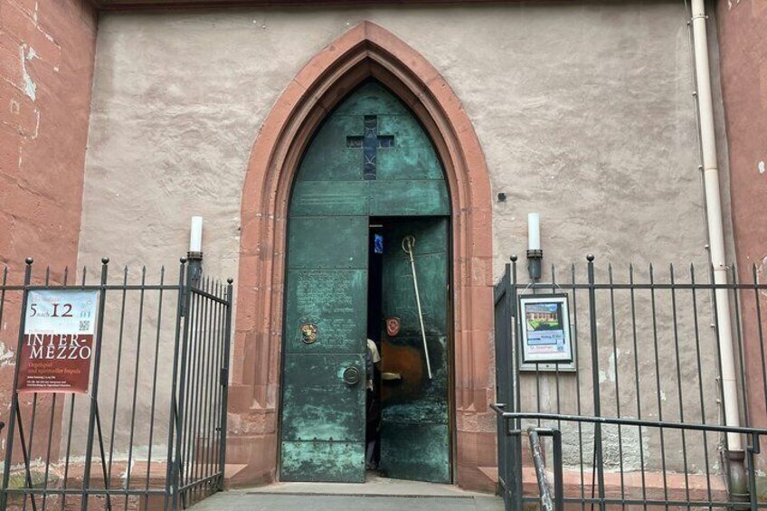 A church entrance with a green door, a cross, and a sign on the left. 2