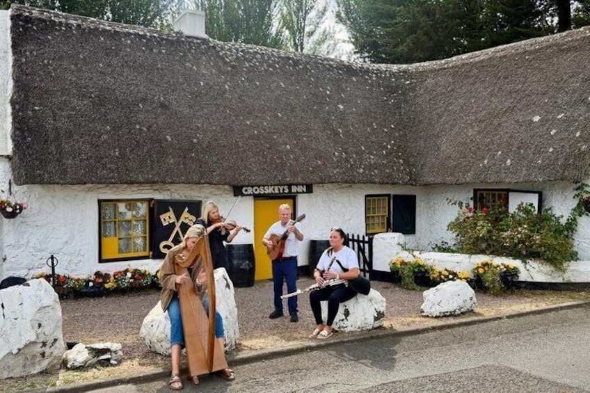 A thatched-roof building with a sign reading 'Crosskeys Inn' and people playing musical instruments outside. 1
