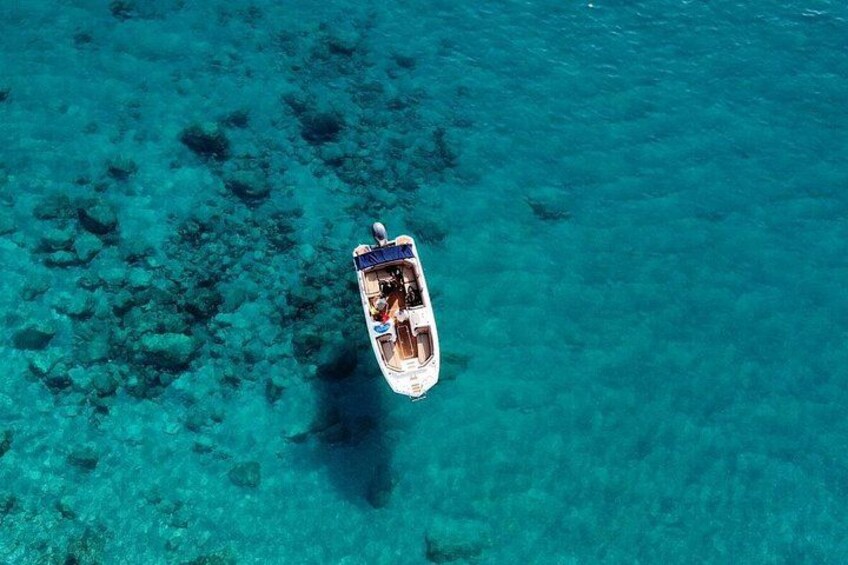 Ein Boot auf klarem türkisblauem Wasser, unterhalb sind Felsen sichtbar. 3