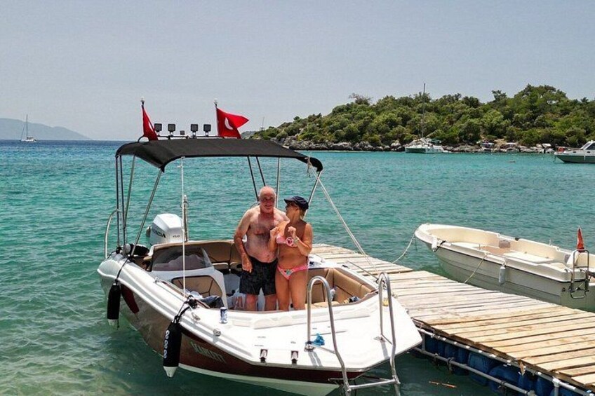 Ein kleines Boot liegt an einem Steg, im Hintergrund eine bewaldete Insel und das klare türkisblaue Meer. 4