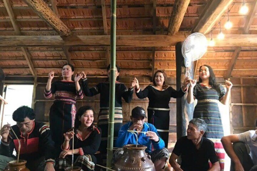 A group of people in traditional attire under a wooden roofed structure, with some holding fans. 2