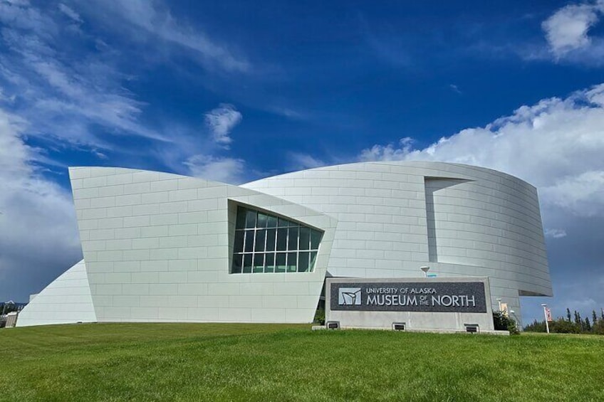 The University of Alaska Museum & North building with a modern design, a large glass window, and a grassy foreground. 1
