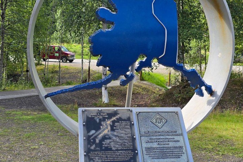 A blue elk sculpture within a circular frame, surrounded by trees and a road with a red vehicle. 5
