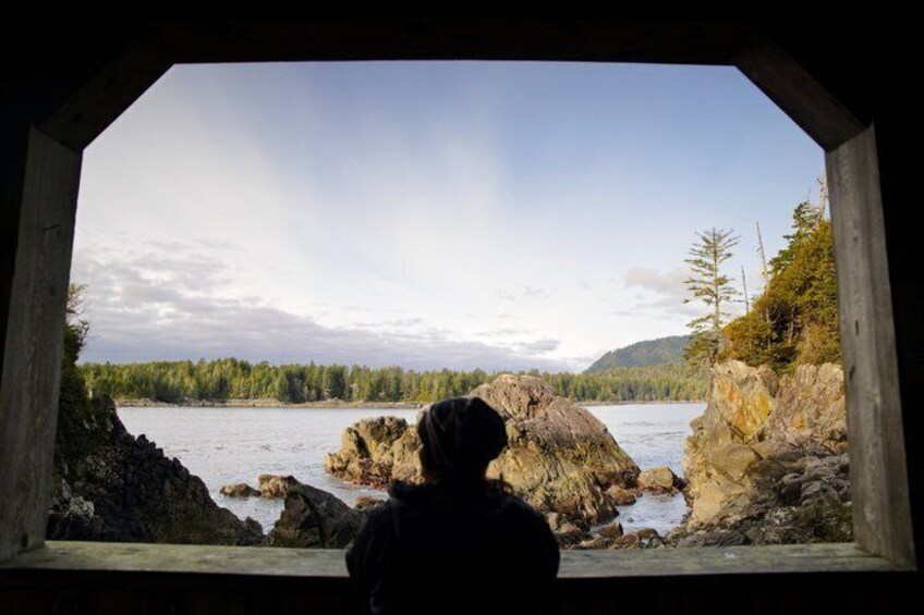 A person looking out from a covered area at a body of water with rocky shores and trees in the background. 5