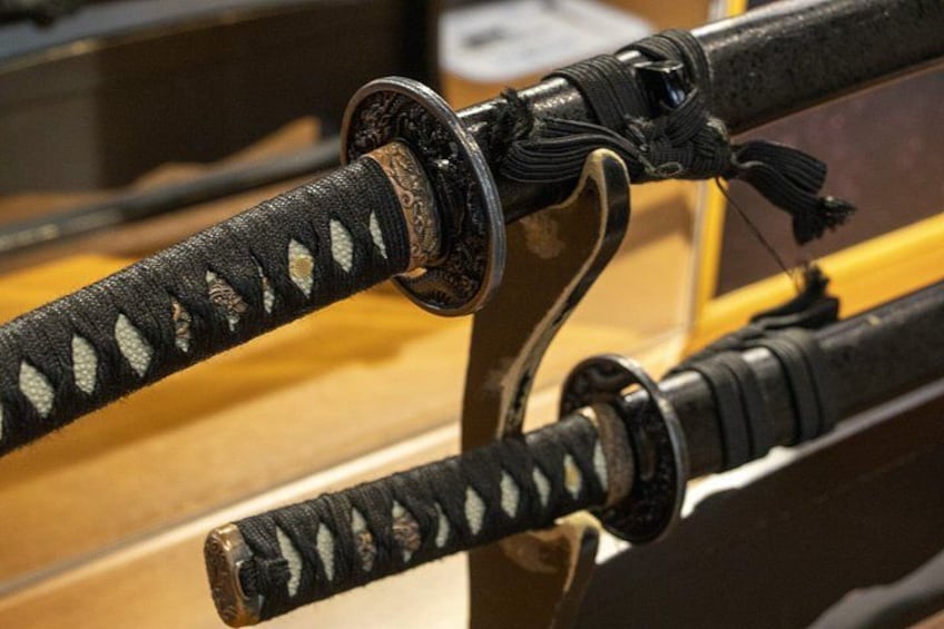 A close-up of three traditional Japanese swords with black sheaths and decorative tassels. 3