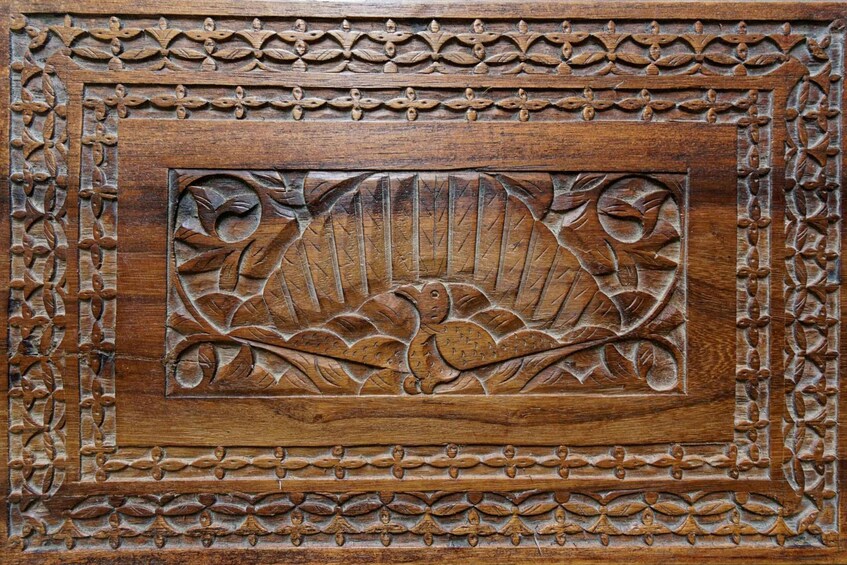 A detailed wooden carving with a central rectangular panel surrounded by a border of leaf motifs. 3