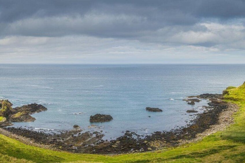 A coastal landscape with rocky shores, grassy areas, and a cloudy sky. 2