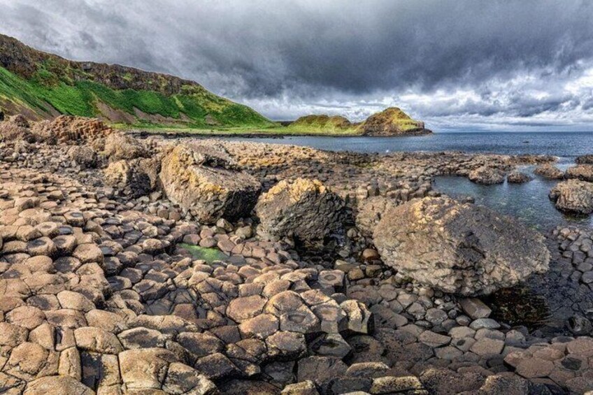 A rocky coastal landscape with large boulders and a distant green hill under a cloudy sky. 5