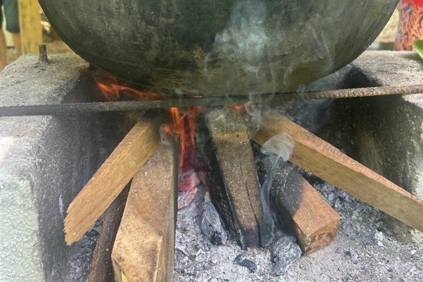 A traditional cooking setup with a large pot over an open fire, surrounded by wooden logs. 3