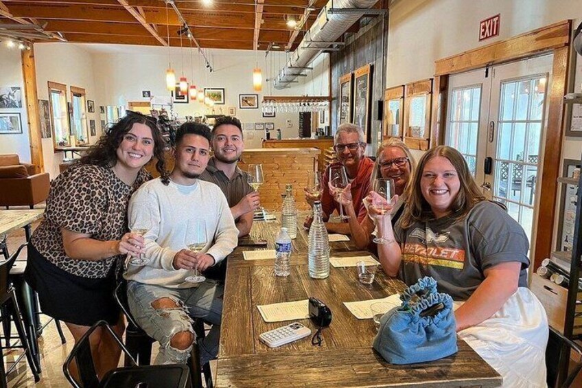 A group of people seated at a wooden table in a restaurant with a bar in the background. 2