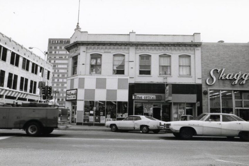 A street with vintage cars parked in front of a building with a sign that reads 'Skaggs.' 3