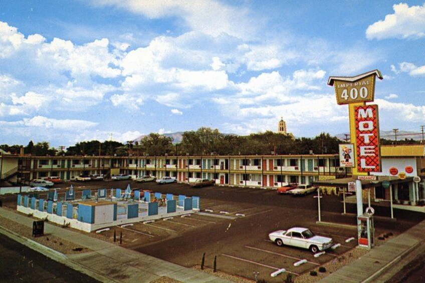 A motel with a large sign, a parking lot, and a road with a car. 2