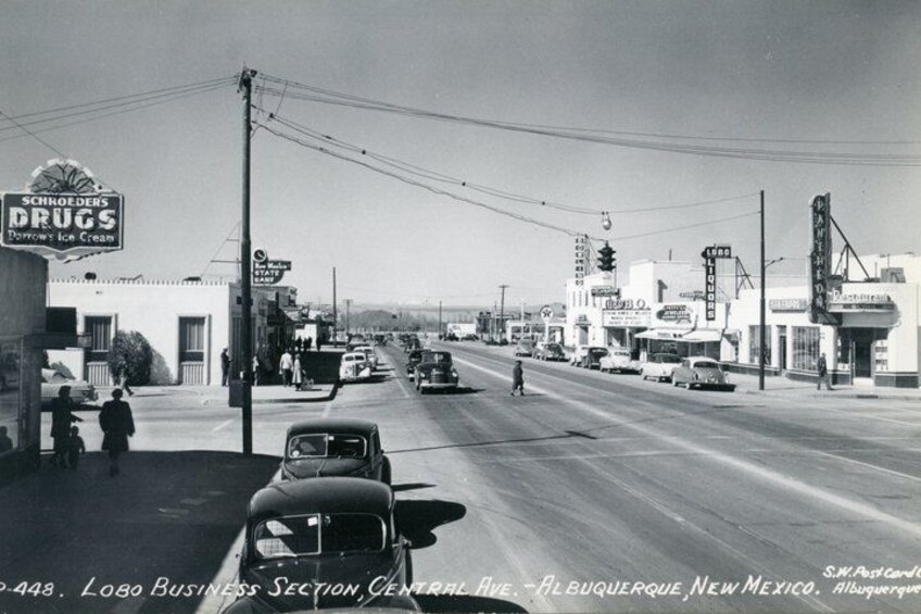 A vintage street scene with cars, buildings, and a prominent drug store sign. 5