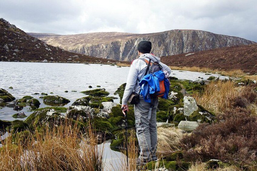 A hiker with a backpack standing by a lake surrounded by rocky terrain and sparse vegetation. 4