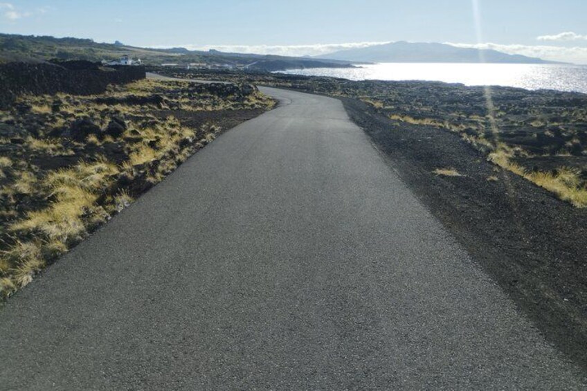 A paved road curving through a barren landscape with volcanic rock and sparse vegetation. 4