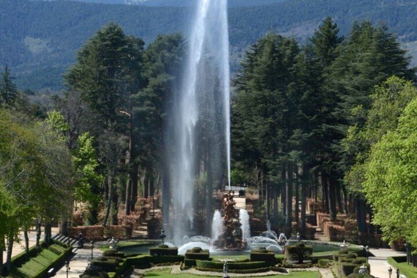 A fountain with water jets in a park with trees and a mountain in the background. 5
