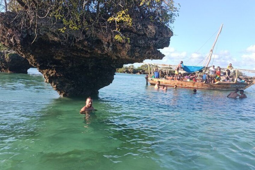 A person swimming near a large rock formation with a boat in the background. 1