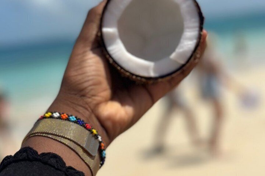 A hand holding a coconut with a beach and ocean in the background. 5