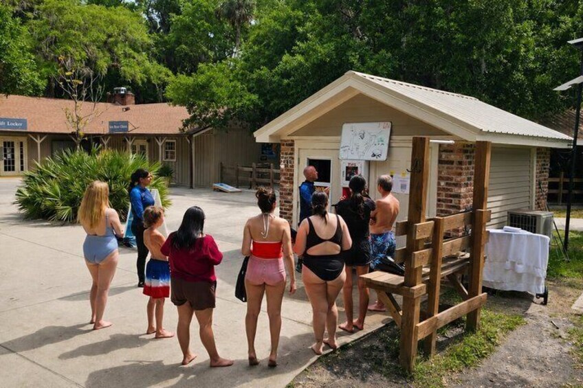 A group of people standing in front of a small building with a map on the wall. 4