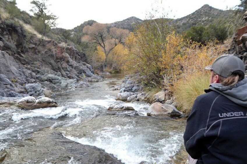 A river with rocks and a person wearing a jacket with 'UNDER' on it. 2