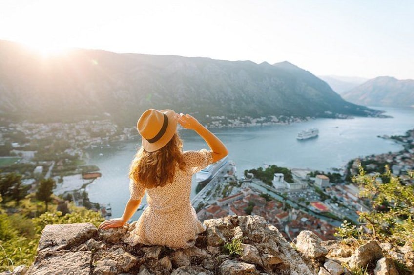 A person sitting on a rock overlooking a lake with a ship in the distance. 1