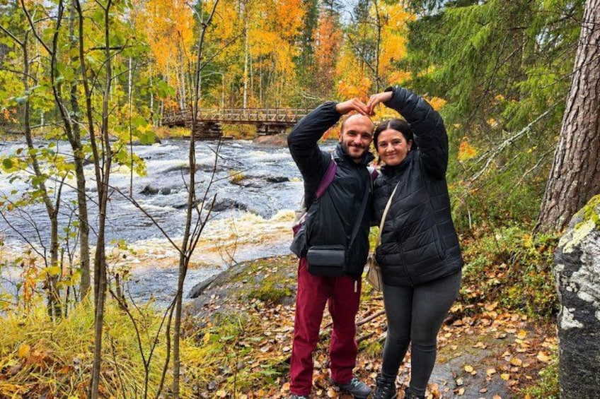 A couple standing by a river with autumn foliage, a bridge in the background, and a rocky terrain. 5