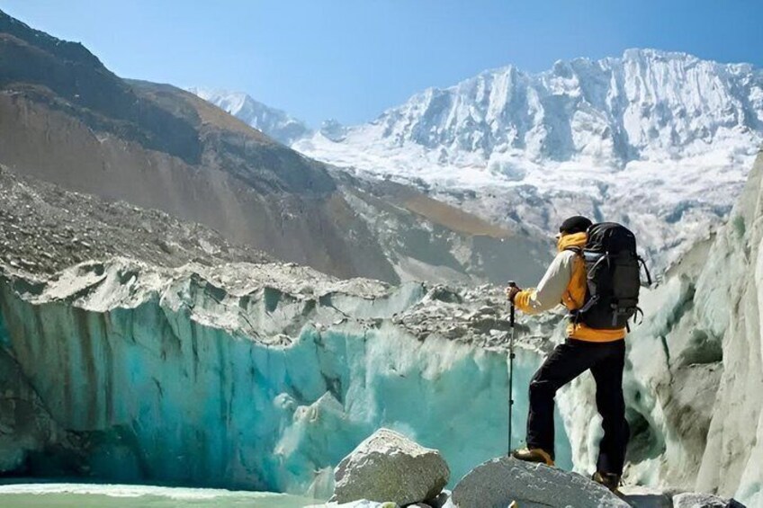A hiker with a backpack standing on a rocky outcrop overlooking a glacier. 3