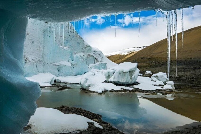 An ice cave with icicles, snow-covered rocks, and a frozen lake. 4