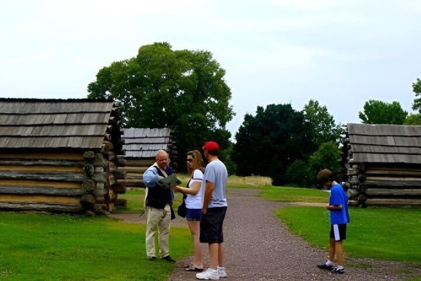 A group of people standing in front of log cabins with a gravel path between them. 3