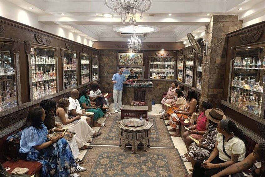 A barbershop with patrons seated on sofas, a counter with a barber, and shelves of grooming products. 2