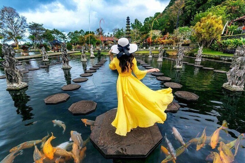 A woman in a yellow dress walking on stepping stones over a pond with fish. 2