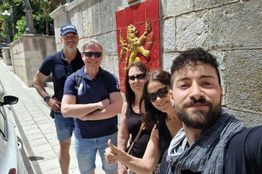 A group of people standing in front of a building with a red door and a golden statue. 3