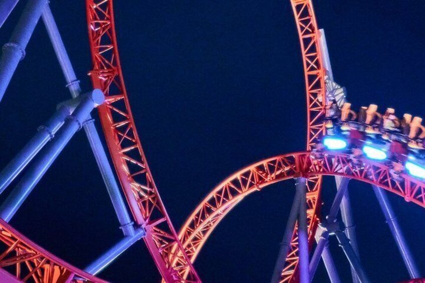 A roller coaster with red and blue lights, steel framework, and passengers. 5