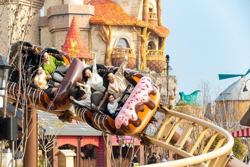 A roller coaster in motion with passengers, a castle-like building, and a windmill in the background. 2