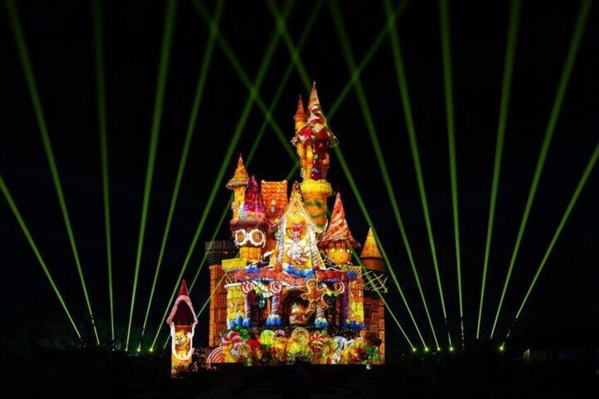 A brightly lit, colorful castle-like structure with multiple towers and a pointed roof, illuminated by green laser lights. 1