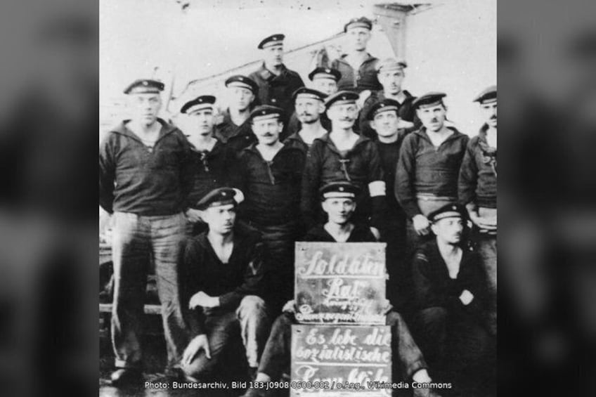 A group of men in uniform standing in a shipyard, holding a sign that reads 'Goldberg Bar.' 5