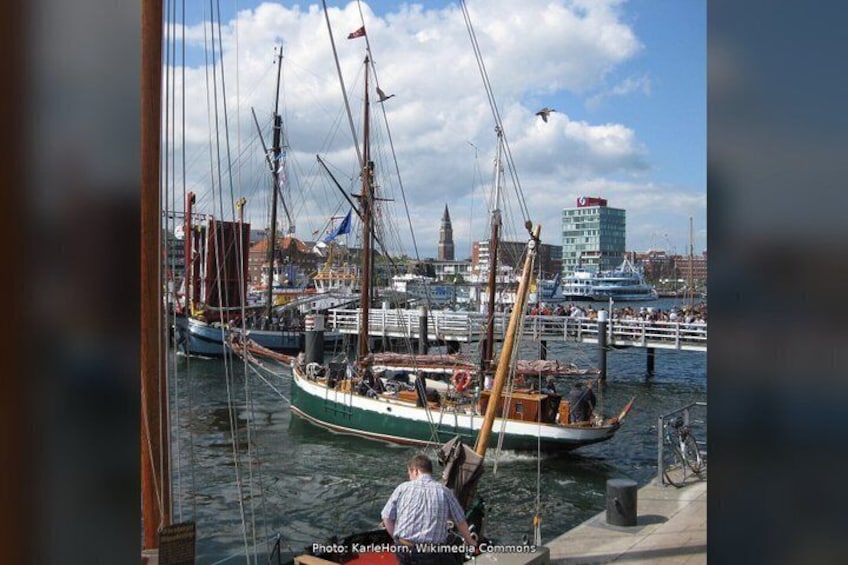 A harbor with sailing boats, a person standing by the water, and a cityscape in the background. 2