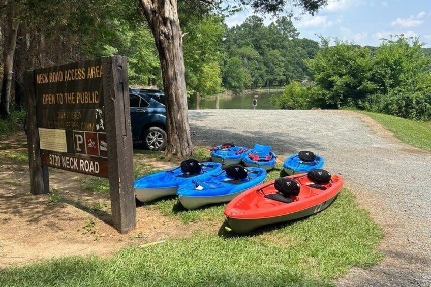 A sign indicating Neck Road Access Area is open to the public, kayaks, and a car parked on a gravel path. 3