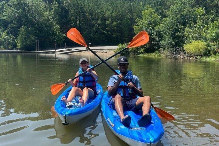 Two people kayaking on a calm river surrounded by greenery. 1